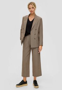 Bruin geruite dubbelgeknoopte blazer en bijpassende wijde broek, gecombineerd met een zwarte gebreide top en zwarte platform sneakers.