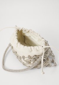 Sac en tissu blanc à cordon de serrage avec un accent en chaîne argentée, présentant un intérieur lisse et une poche zippée. Texture douce et forme arrondie.