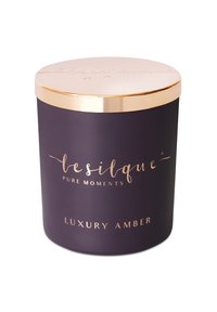 Bocal de bougie cylindrique violet avec un couvercle en métal doré. Présente un élégant gaufrage et un texte indiquant la fragrance "Ambre de Luxe". Texture lisse.