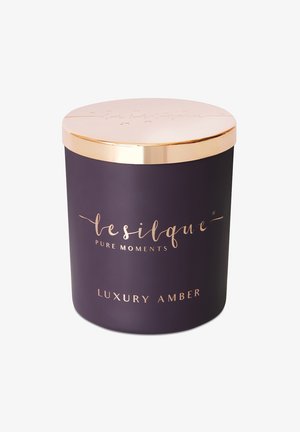 Fioletowy cylindryczny słoik na świecę z złotą metalową pokrywką. Posiada eleganckie tłoczenia oraz tekst wskazujący zapach "Luxury Amber". Gładka tekstura.