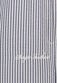 Blårutete og hvitt stoff med myk tekstur, med en brodert logo i kursiv. Stripene er jevnt fordelt og konsistente.