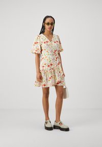 Rochie mini florală cu mâneci bufante, decolteu în V și tiv din straturi, de culoare albă, cu flori portocalii și roz. Purtați cu pantofi cu platformă groasă.
