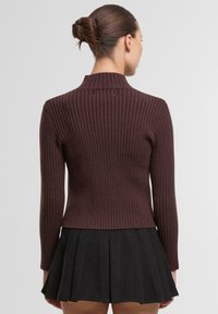 Sweter z prążkowanego dzianiny w ciemnym burgundzie, z wysokim kołnierzem i długimi rękawami, zestawiony z rozkloszowaną czarną spódnicą. Gładka tekstura i dopasowany fason.