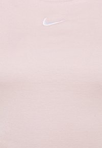 Light pink Nike shirt with a ribbed texture and a small white logo centered on the chest. Classic round neckline.