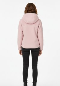 Pink hooded jacket with a textured finish, displayed from the back. Paired with black skinny jeans and ankle boots.