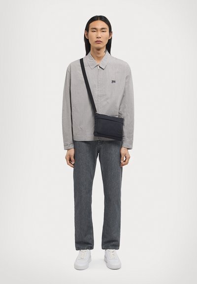 Šedá károvaná košeľa s golierom, v kombinácii s tmavosivými džínami a bielymi teniskami. Z ramena visí kompaktná čierna crossbody taška.