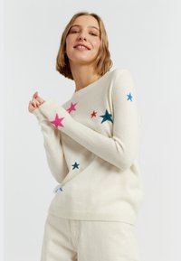 Maglione crema realizzato in morbido tessuto a maglia, con design di stelle multicolori in rosa, blu, verde e rosso su parte anteriore e maniche.
