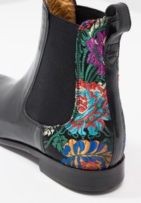 Bottine en cuir noir avec panneau latéral élastique et broderie florale colorée à l'arrière et sur le talon.