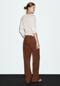 Beżowy top z długim rękawem i ściągaczami, zestawiony z brązowymi surowymi spodniami w stonowanej linii, prezentującymi gładką strukturę i dopasowany krój.