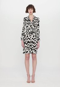 Rochie cu model alb-negru, cu maneci lungi, închidere cu nasturi și talie legată, având un design geometric în zigzag. Material neted.