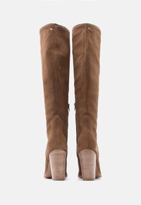 Ψηλές καφέ μπότες από σουέντ με χοντρούς τακούνια, ορατό φερμουάρ στην εσωτερική πλευρά και λεπτομέρειες ραφής στην πίσω πλευρά.