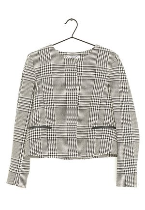 Veste à manches longues à motif pied-de-poule en noir et blanc, avec encolure ronde et deux poches avant zippées, suspendue à un cintre noir.