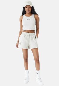 Hellgraues, kurzes Tanktop und passende Shorts mit Kordelzug. Weiße Logo-Accents und weiße Sneakers. Getragen mit einer passenden Mütze und Socken.