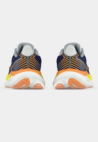 Modré a oranžové bežecké topánky z pohľadu zozadu, ukazujúce vypchávky sivej farby a biele podrážky s oranžovými vzormi.