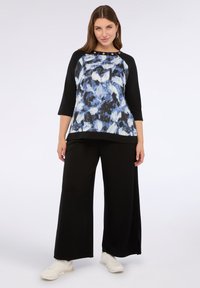 Maglietta a maniche lunghe con un motivo astratto blu e nero, maniche nere e bottoni decorativi sul colletto, abbinata a pantaloni neri a gamba larga.