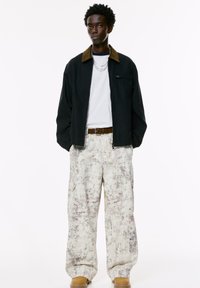 Black zip-up jacket with brown collar, white t-shirt, oversized speckled beige cargo pants, and brown boots. Two silver chains as accessory.