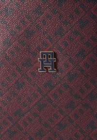 Portefeuille en cuir avec un motif rouge et noir, au fini texturé, avec un logo en émail marine accentué par des accessoires en or.