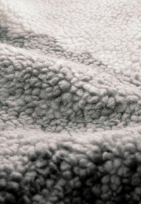 Miękki, teksturowany szary i biały materiał polarowy z falistym wzorem, prezentujący pluszowy i przytulny wygląd.