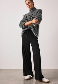 Gray, fuzzy pullover with a half-zip and black lettering, paired with black loose-fit pants and white sneakers with brown soles.
