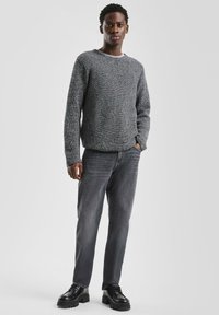 Grijze gebreide trui met een ronde hals; gecombineerd met donkergrijze straight-leg jeans en chunky zwarte schoenen. Vlak, glad oppervlak, casual pasvorm.