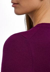 Maglione viola vibrante che mostra una maglia strutturata, scollo rotondo e maniche raglan, con cuciture visibili che confermano i dettagli del design.