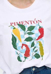 Camiseta blanca con gráficos coloridos de pimientos en rojo, amarillo y verde sobre un fondo de cuadros azul claro con la palabra "PIMENTÓN."