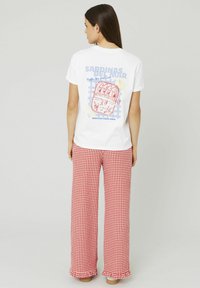 T-shirt blanche avec une impression graphique bleue et rouge au dos, associée à un pantalon large à carreaux vichy rouge et blanc. Texture de tissu lisse.