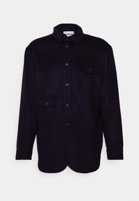 Dark purple shirt in soft fabric featuring a button-down front, collar, and two chest pockets with button closures. Curved hem design.