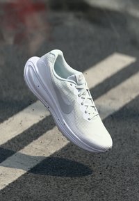 White athletic shoe with a textured mesh upper, a rounded silhouette, and a light grey Nike swoosh logo on the side. Lightweight sole design.