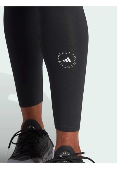 Zwarte sportleggingen met een slim fit ontwerp, voorzien van een cirkelvormig wit logo op de linker kuit en een gladde, rekbare textuur.