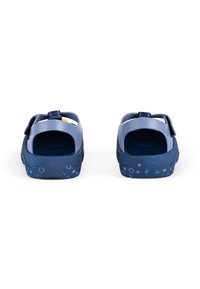 Blaue Sandalen mit offenem Rücken, aus Kunststoff gefertigt. Sie verfügen über eine strukturierte, dunkelblaue Sohle mit dekorativen, hellblauen Kreisen und einem Klettverschluss.