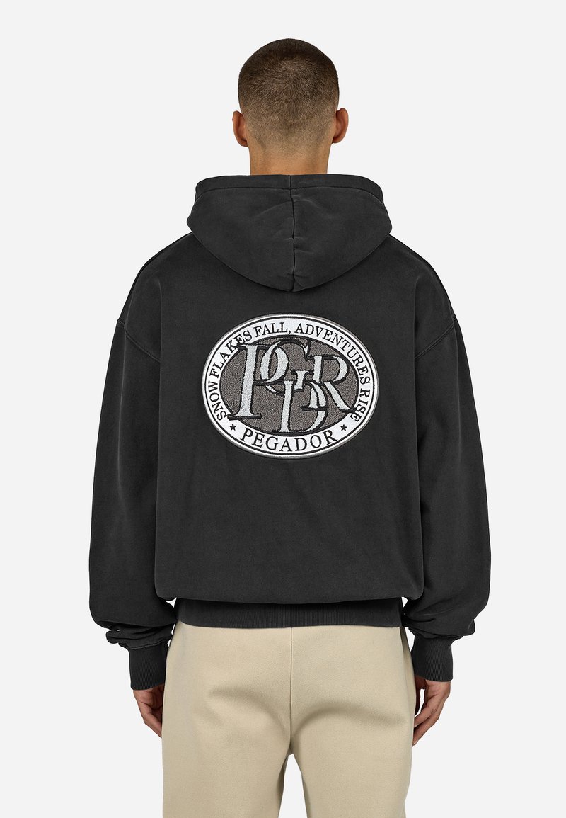 Čierna mikina s kapucňou so sťahovacou šnúrkou, na zadnej strane s veľkým kruhovým vyšívaným logom a textom a grafickými detailmi. Voľný strih.