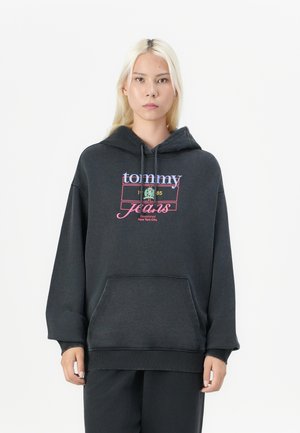 Čierna oversized mikina s kapucňou a predným vreckom, s farebným nápisom "tommy jeans" a šnúrkou na kapucni. Jemná, textúrovaná látka.