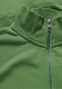 Grüne Zip-Hoodie mit hohem Kragen, gerippter Textur und silbernem Reißverschluss. Der Stoff wirkt weich und glatt, entworfen für Komfort.