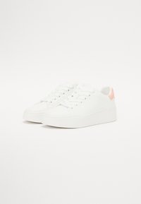 Sneakers bianchi con superficie liscia, punta arrotondata, suola piatta e un'accento rosa chiaro sul tallone. Lacci e occhielli per una vestibilità sicura.