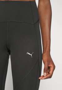 Leggings negros de cintura alta con una textura suave, que presentan un logo reflectante en plata de Puma en el muslo y detalles de costura en contraste.