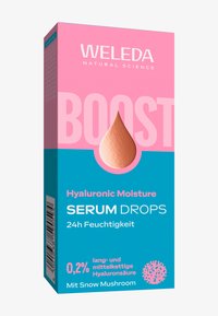 Opakowanie serum nawilżającego Weleda z kwasem hialuronowym ma różowo-niebieskie pudełko z okienkiem w kształcie kropli, za którym widać jasno-brązowe serum w środku.