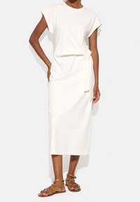 Biała midi sukienka z miękkiego materiału, z krótkimi rękawami i wiązaniem w talii. Noszona z brązowymi sandałami na paski.