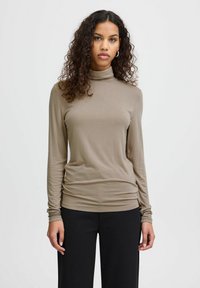 Blusa de manga larga y cuello alto en color beige, hecha de una tela suave y elástica con una silueta ajustada y detalle fruncido en el costado.