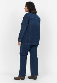 Temno modra denim jakna in hlače s sproščenim krojem, vidnim šivanjem in gumbnimi akcenti. Težka tkanina z gladko teksturo.