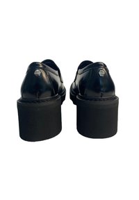 Scarpe in pelle nera con tacco a blocco, caratterizzate da una finitura lucida, punta arrotondata e suola nera testurizzata a contrasto. Dettaglio del logo esagonale visibile.