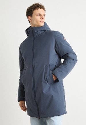Parka acolchada azul marino con cierre de cremallera, capucha con cordón, bolsillos laterales y parche de logo en la manga. Textura suave y corte ligeramente holgado.
