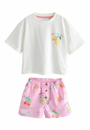 Gyerek fehér, túlméretezett pólót visel, nyári témájú mintákkal, valamint rózsaszín rövidnadrágot jégkrém és desszert mintákkal, háttal áll.