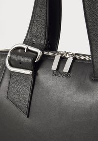 Black leather handbag with textured surface, silver hardware, and dual zippers. Features embossed "HUGO" logo on the side.