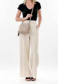 Borsa a tracolla trapuntata beige con hardware argentato, indossata con una maglietta nera a maniche corte e pantaloni palazzo beige chiaro. Sandali neri flat.