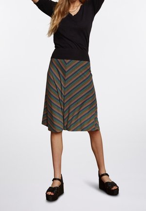 Mustat neulepusero V-pääntiellä yhdistettynä moniväriseen viuhkakuosiseksi hameeseen. Mallilla on päällään mustat platform-sandaalit.