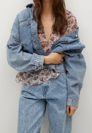 Kvinde iført lyseblå oversized denimjakke og jeans med en blomstermønstret bluse under.