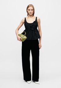 Top negru cu peplum și aplicații florale, asortat cu pantaloni negri largi. Modelul ține o geantă mică verde și poartă tocuri albe ascuțite.