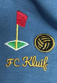 Het geborduurde logo op de blauwe stof toont een rode vlag op een groene golftee en een gestileerde zwarte en gouden volleybal met "FC Kluif" in goud eronder.