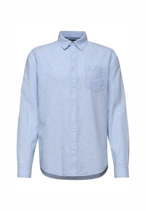 Homme en chemise bleu clair à boutons avec poche poitrine, regardant vers la gauche sur un fond neutre.